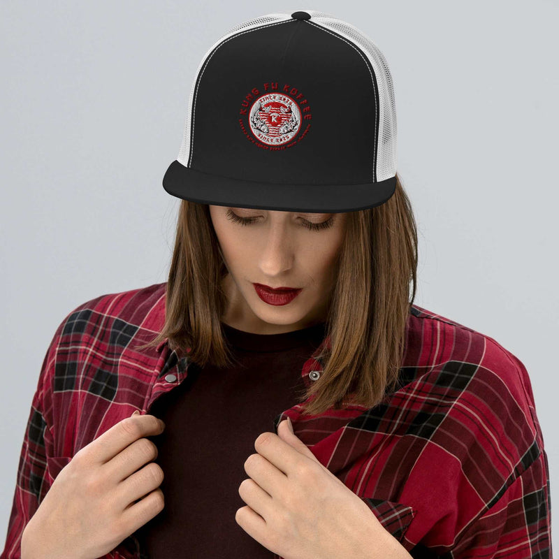 Black and white structured trucker cap with red logo patch worn by woman in red plaid shirt